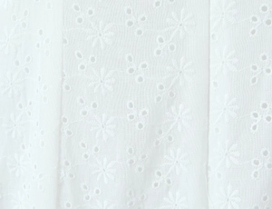 Detailed close-up of white floral embroidery fabric with refined hollow-out geometric patterns