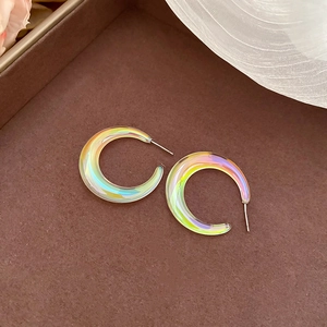 Detailed close-up of iridescent C-shaped acrylic earrings on a brown display tray