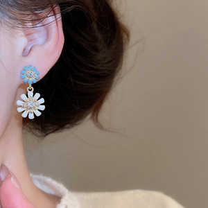 Close-up of floral drop earrings with blue and white petals and crystal center on model