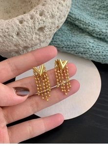 Detail of hand-held gold V-shaped chain tassel earrings with polished metallic finish