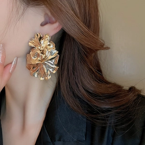 Detailed close-up of oversized gold floral fan earrings with wrinkled metal texture