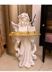 Detail of a vintage angel statue holding a gold metal tray for home decor storage