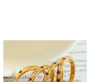 Macro shot of gold rings with colorful inlaid crystals on white ceramic background