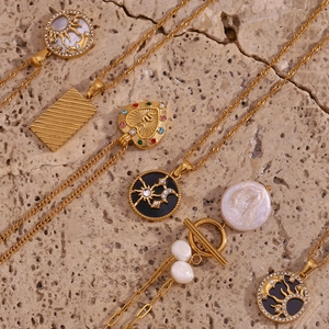 Macro shot of gold plated necklaces with sun, moon, heart charms and pearls on stone