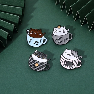 Close-up of four cute enamel cat pins in teacups set against a green paper background