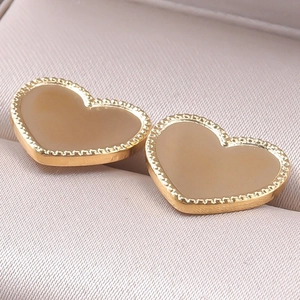 Close-up of heart-shaped gold studs with beige inlay and beaded metal edges on velvet