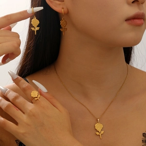 Macro detail of a minimalist gold rose jewelry set featuring a necklace, earrings, and ring