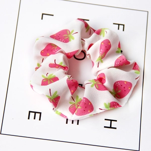 Close-up of white chiffon scrunchie featuring vibrant red strawberry patterns on a display card