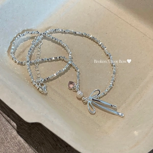 Detail of necklace with broken silver chain, pink heart gem, pearl and bow charm