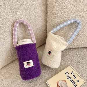 Detalle de bolsas de felpa suave para botellas en morado y crema con asas de cuadros