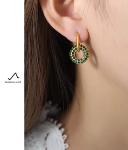 Close-up of gold stainless steel huggie earrings with a green pave-set round pendant