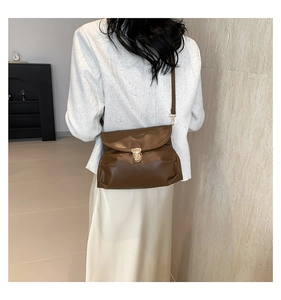 Detail view of deep brown faux leather shoulder bag with gold circular metal clasp on model