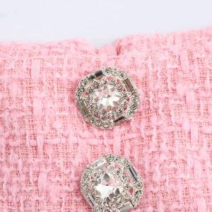 Details einer rosa Tweed-Jacke mit zwei glitzernden Strassknöpfen und Fransen-Design