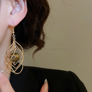 Close-up of a model wearing twisted gold diamond-shaped earrings with brown tiger eye beads