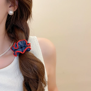 Detail of denim hair scrunchie with red piping worn on a low ponytail by model