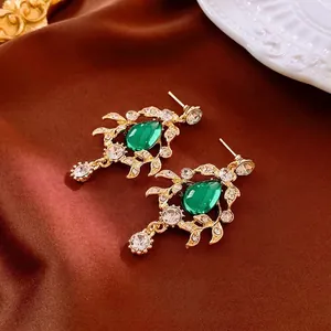 Vintage gold leaf earrings with pear-shaped green gemstones and white diamonds on satin