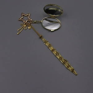 Detail of a golden bag charm with a small mirror, metal tassels and star pendants