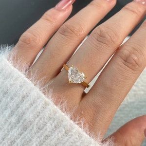 Close-up of heart-cut clear gemstone ring with gold-tone prong setting on a white sweater