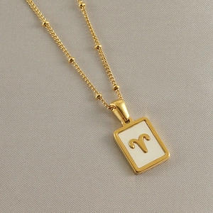 Close-up of 18k gold Aries zodiac pendant necklace with white shell on grey fabric