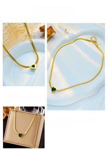 Detail of gold snake chain necklace featuring a green heart pendant and adjustable clasp