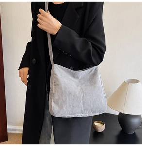 Detail of grey corduroy crossbody bag texture and outer pocket on model in black suit