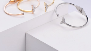 Three dolphin tail bangle bracelets in rose gold, gold, and silver with zircon accents