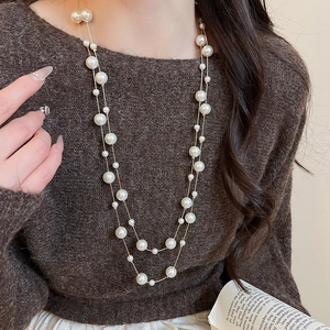 Detail of layered white pearl necklace with gold chain on dark brown sweater