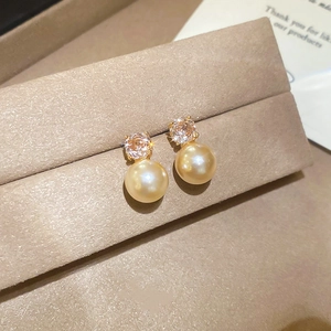 Macro detail of gold-plated pearl earrings with sparkling champagne zirconia setting