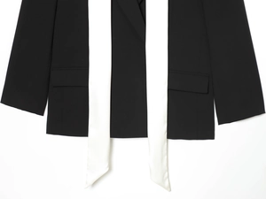 Detail of minimalist black blazer with contrasting white long scarf and flap pockets