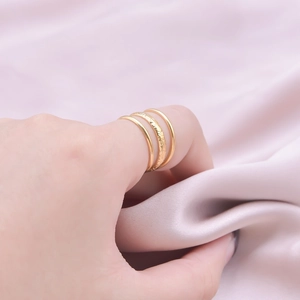 Macro shot of three stacked golden steel rings featuring a hammered texture on pink silk