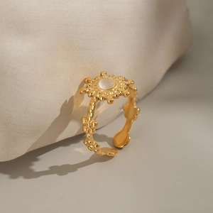 Macro shot of gold sun-shaped open ring featuring white stone and floral relief