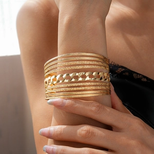 Detail showing a layered stack of gold bangles including curb chain and matte finish rings