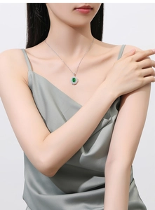 Detail of silver halo necklace with oval green gemstone worn by a model in silk top
