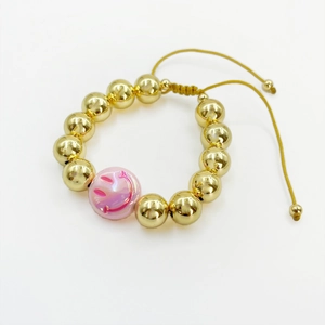 Macro detail of 18k gold plated beaded bracelet with purple smiley face charm