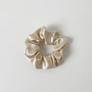 Detailed close-up of champagne gold satin scrunchie with soft silk texture and pleats
