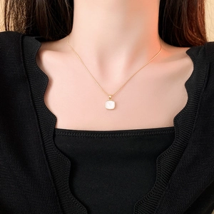 Détail du pendentif carré en nacre blanche sur une chaîne en acier titane doré
