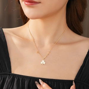 Close-up of a gold beaded chain necklace with a sparkling four-leaf clover pendant on a model