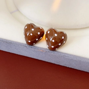 Close-up of brown heart-shaped stud earrings with white polka dots on a display stand