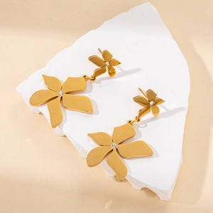 Golden five-petal flower earrings with a center zircon on a textured stone background