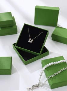 Macro view of green textured jewelry boxes featuring elegant swan pendant necklaces