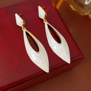 Close-up of white enamel teardrop earrings with gold edges on a rustic wooden box