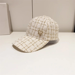 Detail of tweed baseball cap featuring gold thread texture and pearl heart accent