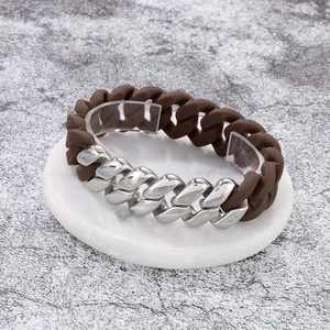 Close-up of brown silicone and silver metal Cuban link bracelet on marble stand