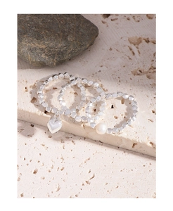 Close-up of three silver beaded rings featuring a heart charm and a white pearl on a stone slab
