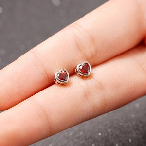 Macro shot of small silver stud earrings with vibrant red heart-shaped gemstones held by hand