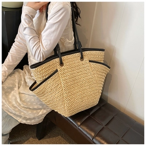 Detail of a large beige woven tote bag with black handles held by a model for a beach look