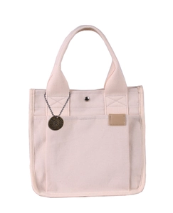Detailaufnahme der cremefarbenen Canvas-Tasche mit Metallanhänger und Lederetikett