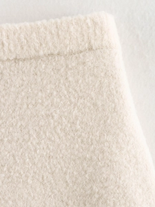 Close-up of the off-white bouclé knit texture and woven edge details of the garment