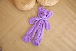 Detail of a large purple teddy bear skin with a silk bow on light wood flooring