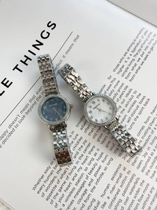 Detail of silver ladies watches with diamond bezels on book pages, blue and white dials